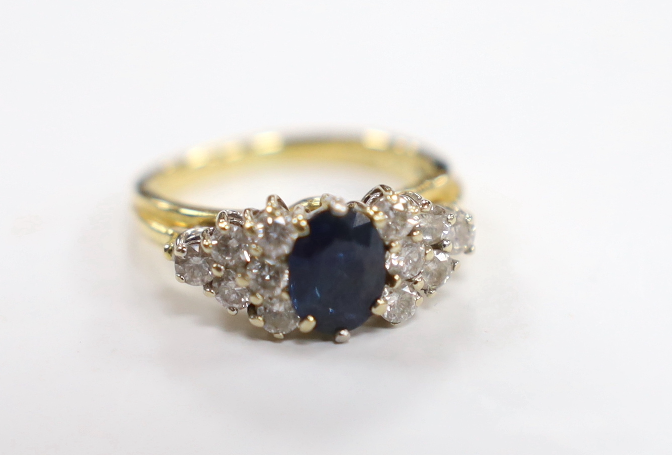 A modern 18ct gold and single stone oval cut sapphire set dress ring, with twelve stone diamond set shoulders, size O, gross weight 6.7 grams.